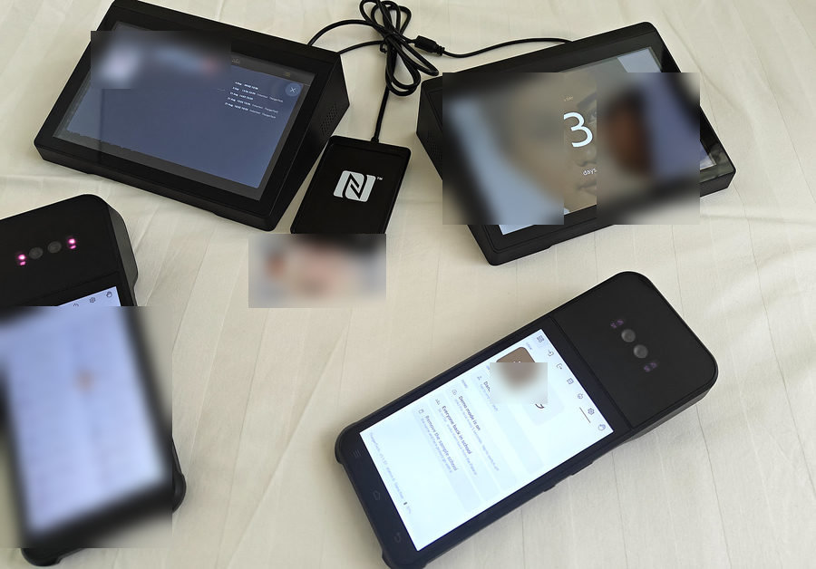 The kit on a desk: one front desk showing a visitor's record, the other the notice board, the Emirates ID reader and card, and two handheld palm readers